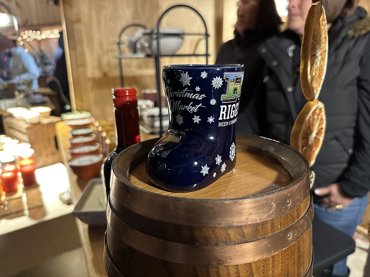 A Christmas Market at a brewery. A small, ceramic decorative boot with Riggs' logo on it is on top of a small wooden barrel. The shop has lots of other items for sale in the background. Photo by Jake Williams. 