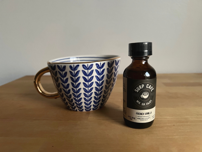 On a wooden counter, there is a decorative mug beside a brown bottle of cannabis infused syrup called Surp. Photo by Alyssa Buckley.