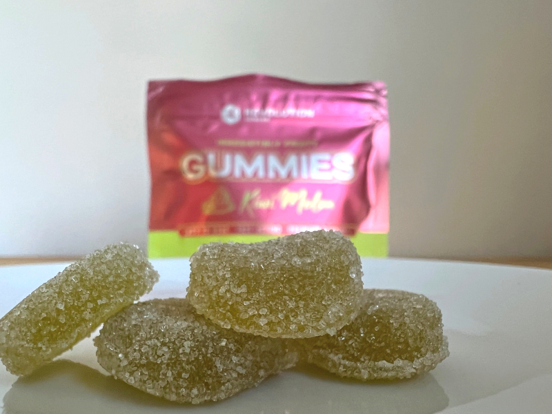 On a white plate, there are four yellow-green gummies in front of the pink bag. Photo by Alyssa Buckley.