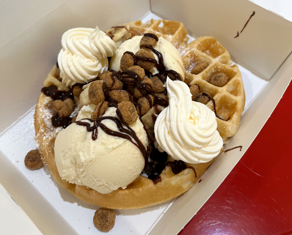A waffle with ice cream, cereal, bananas, whipped cream, and chocolate drizzle in a take-out container. Photo by Jessica Hammie. 