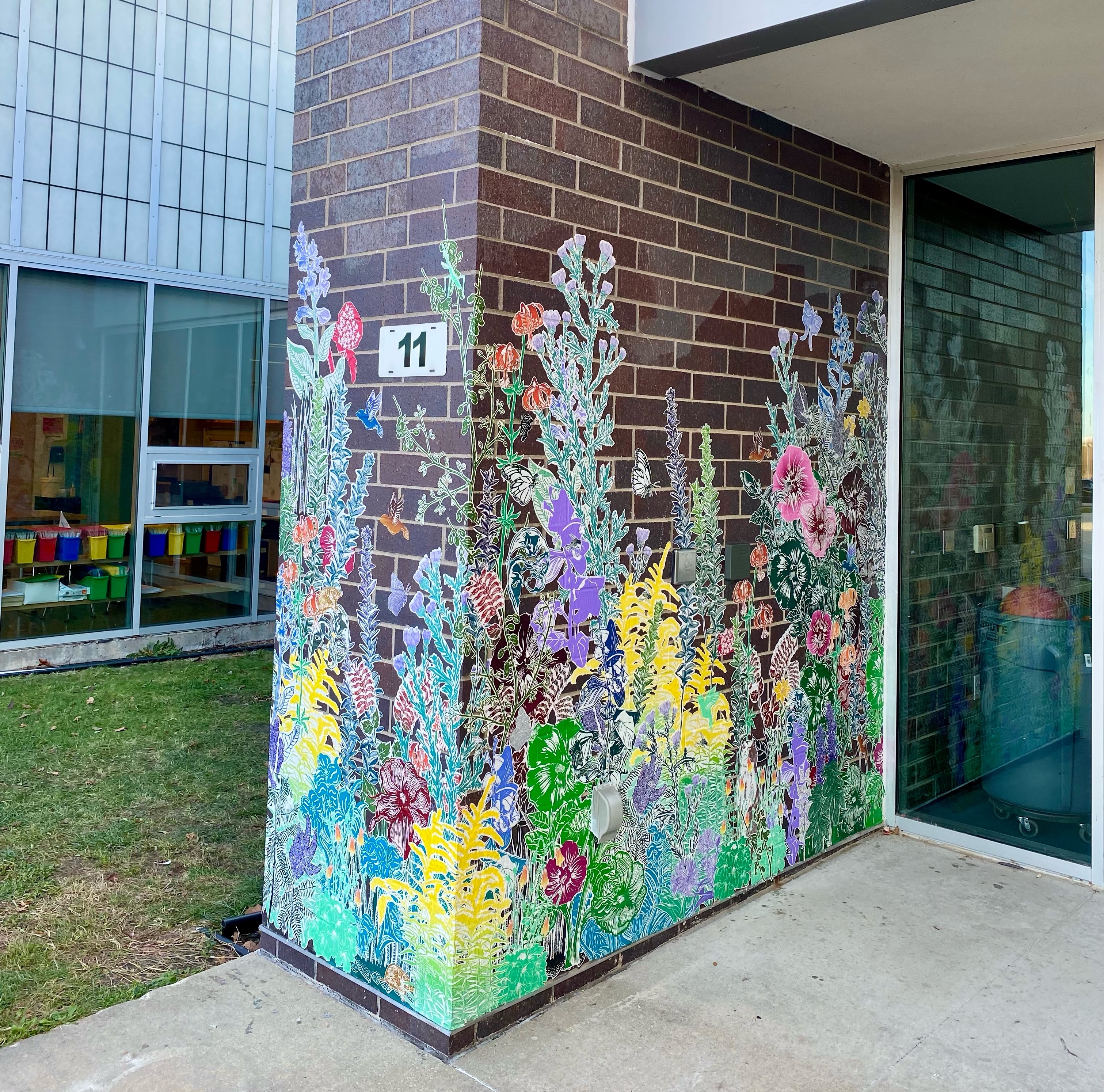 A colorful paste-up installation of various plants is on a brick wall at Carrie Busey Elementary school. The prinstallation wraps around the wall to the other side. Photo by Emmy Lingscheit.