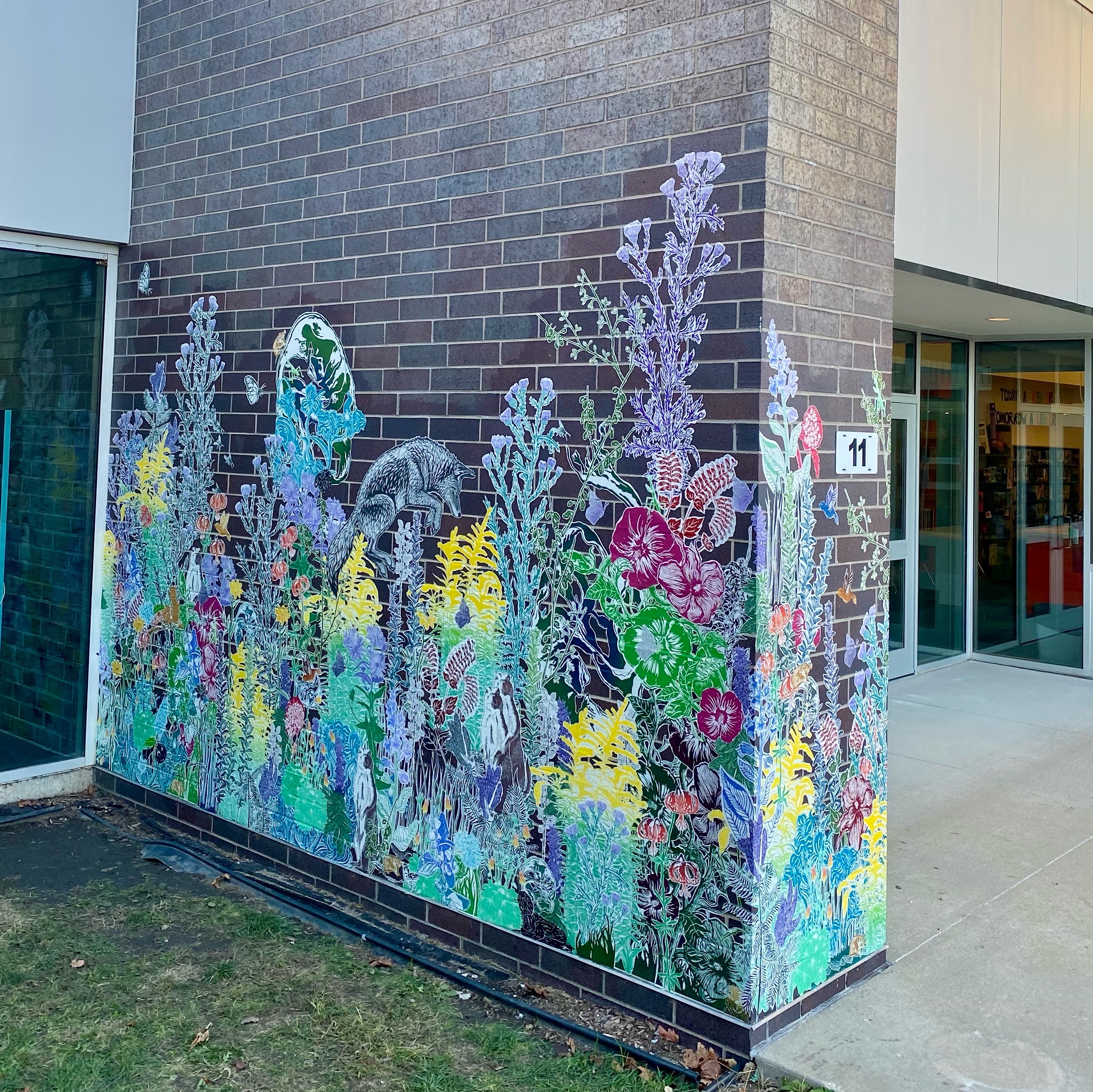 A colorful paste-up installation of various plants is on a brick wall at Carrie Busey Elementary school. The prinstallation wraps around the wall to the other side. Photo by Emmy Lingscheit.