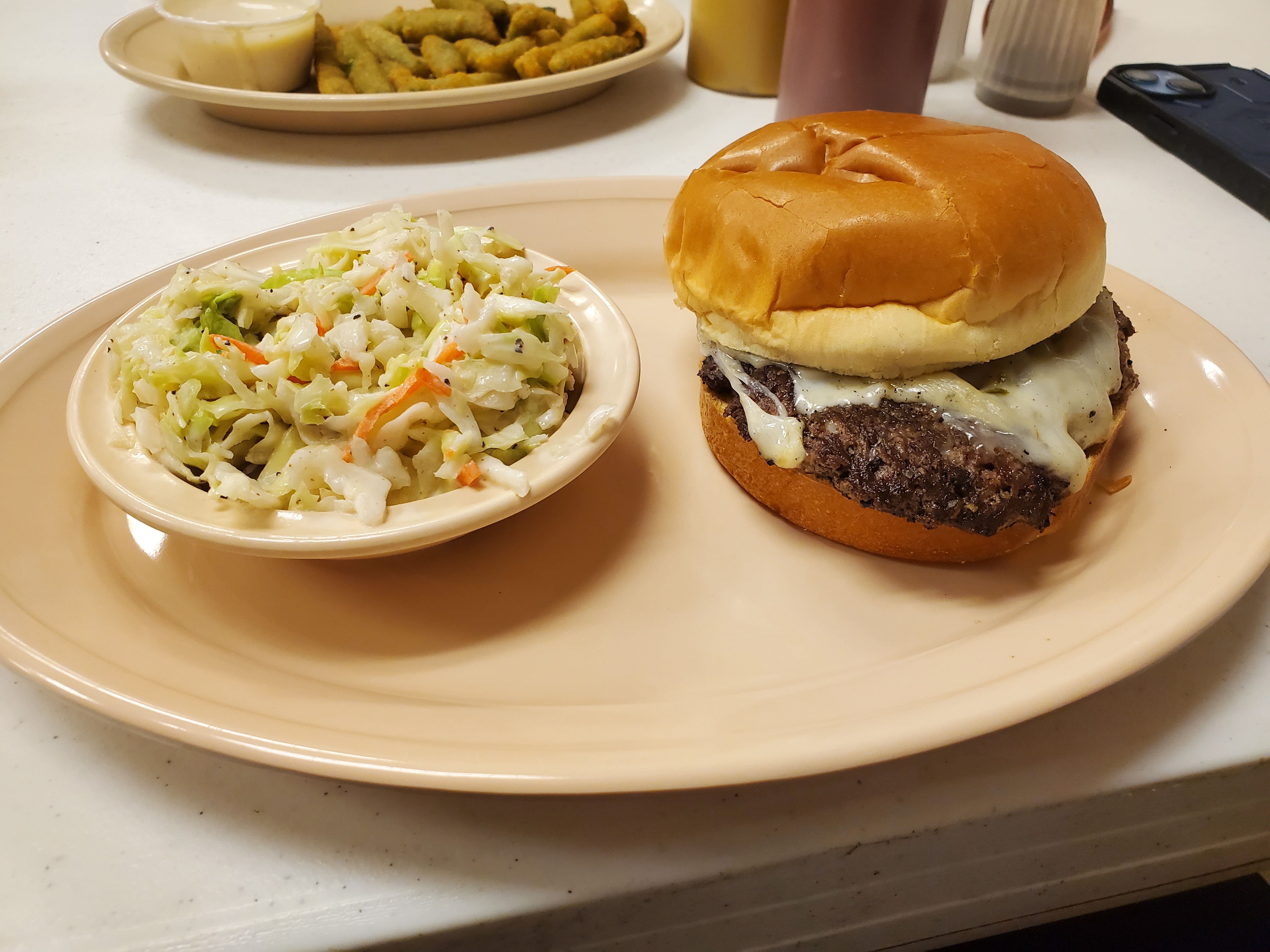On an oval plate, there is a cheeseburger and a bowl of slaw. Photo by Carl Busch.