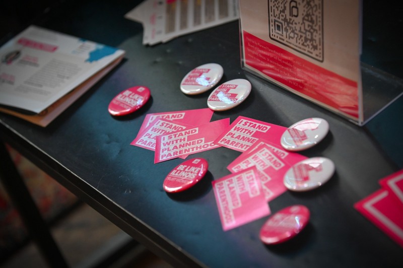 Close up of a display table. There are pink Planned Parenthood buttons and stickers scattered on it. Photo from Planned Parenthood Action of Illinois.