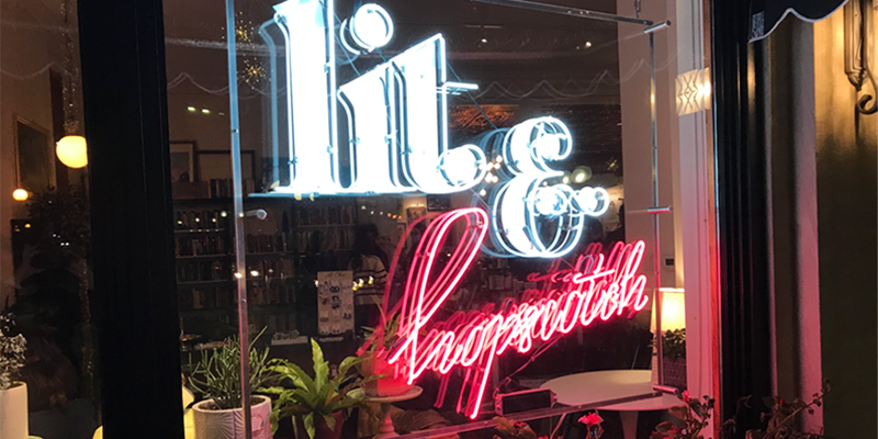 Front window of The Literary Bookbar with the words â€œThe Litâ€ and â€œHopscotchâ€ in neon letters. Photo by Kathleen McGowan.